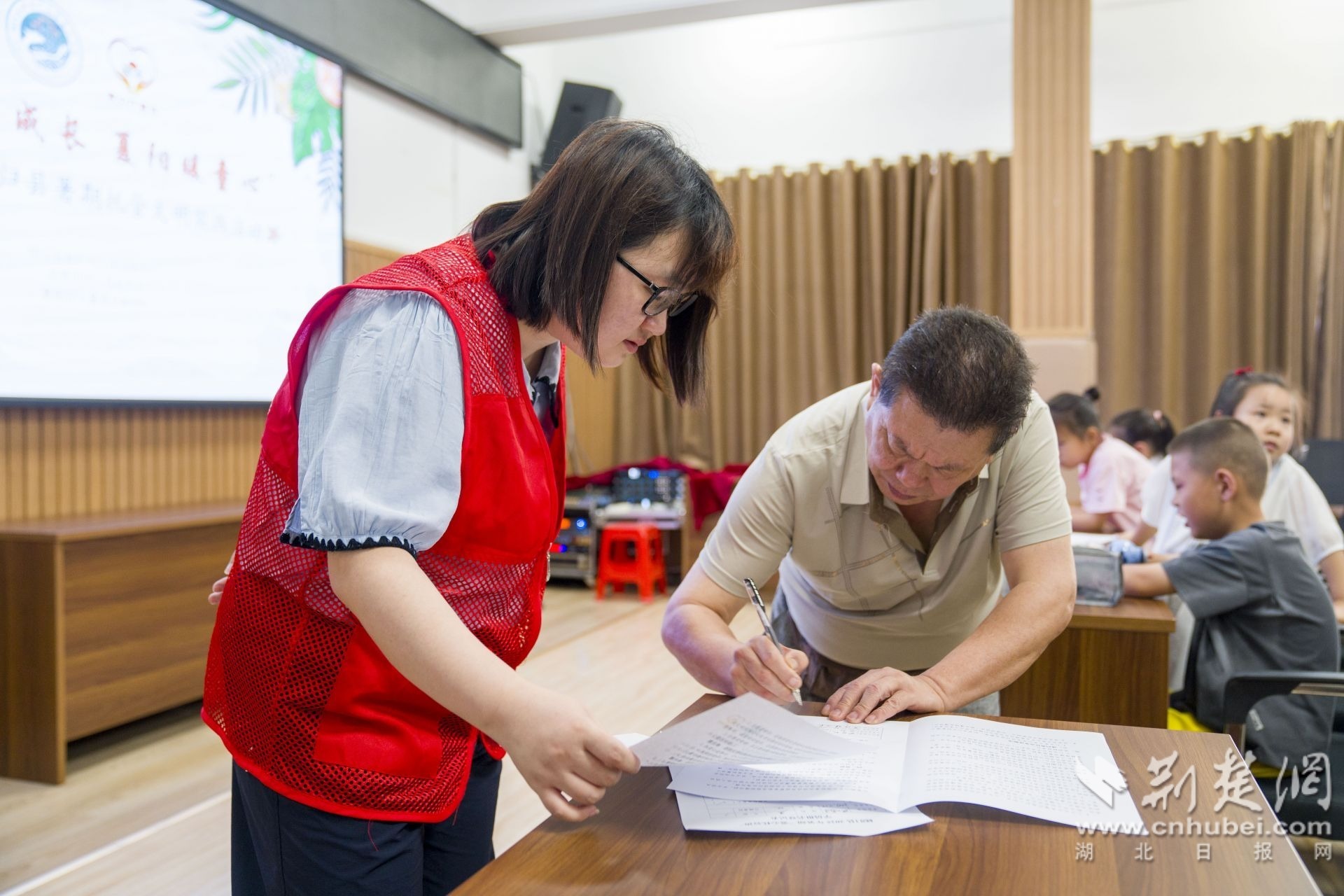 7月5日，在秭归县新时代文明实践中心暑期托管班志愿者指导家长填写报名表。 周仕伟 摄.jpg.jpg