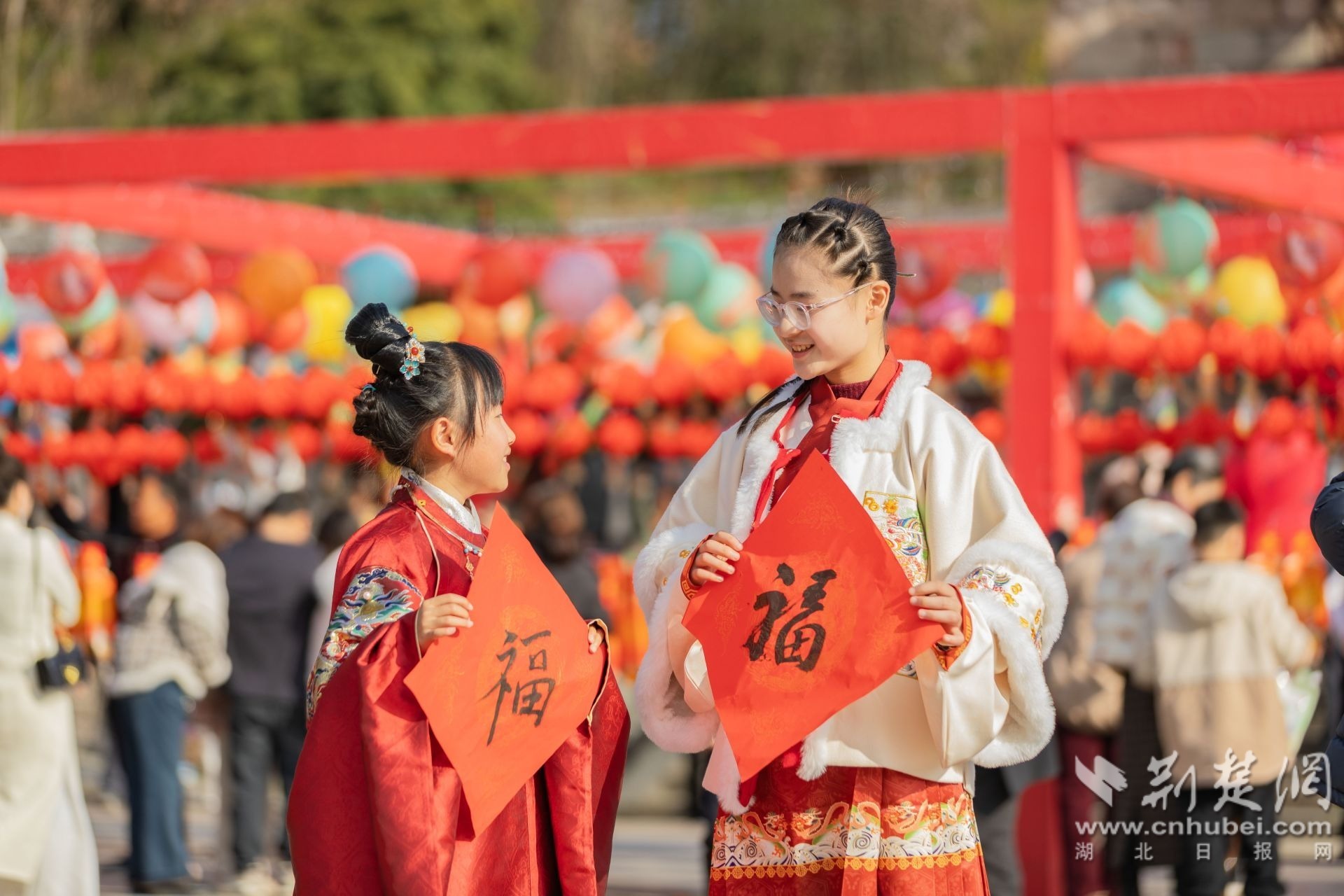 2026年3月3日，在湖北省宜昌市秭归县屈原故里南门广场，两位身着传统汉服的小朋友在热闹的元宵市集里，集福贺春，尽显节日的喜庆与